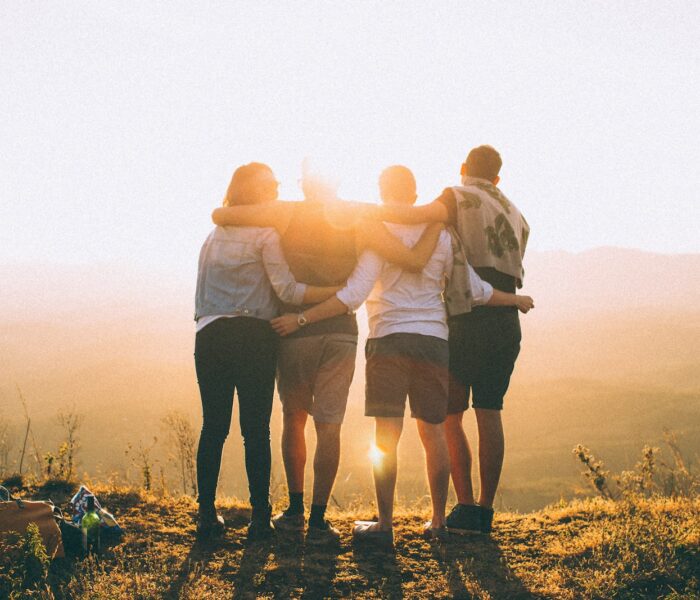 four person hands wrap around shoulders while looking at sunset