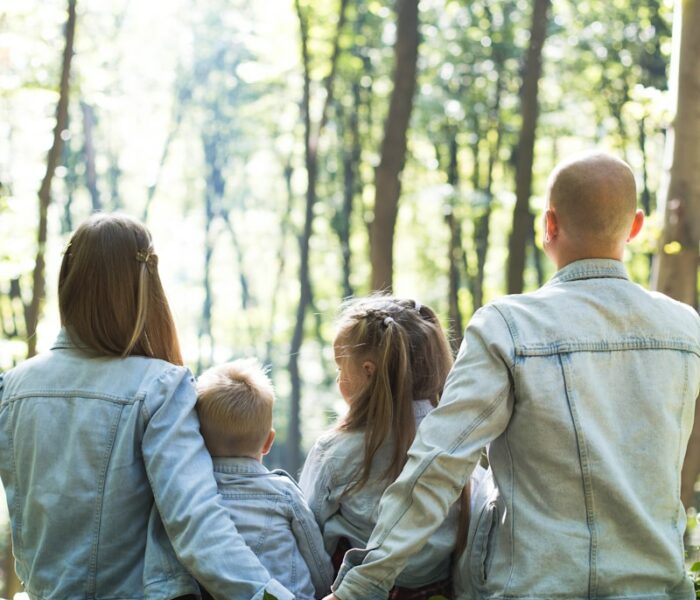 man and woman holding hands together with boy and girl looking at green trees during day
