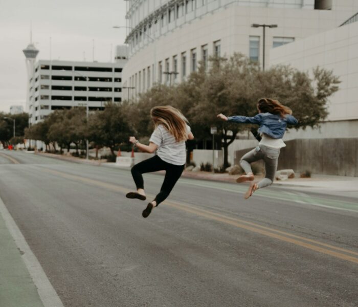 two woman jumping on the street during daytime